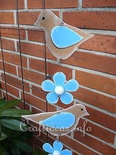 two blue birds hanging from a wire next to a brick wall with flowers on it