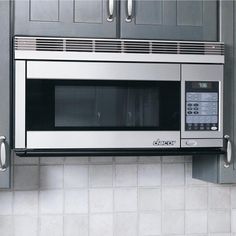 a stainless steel microwave oven mounted on the wall in a kitchen with gray cupboards