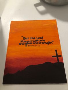 a painting on a table with a cross in the foreground and an orange sky behind it