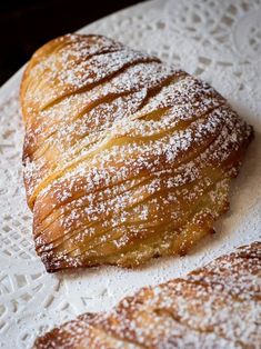 two croissants sitting on top of a white plate covered in powdered sugar