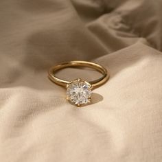 a gold ring with a single diamond on top of a white cloth covered bed sheet