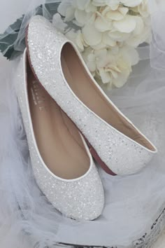 white wedding shoes with silver sequins on them and flowers in the back ground