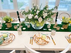 a table set with place settings and flowers in vases on the centerpiece, along with green napkins