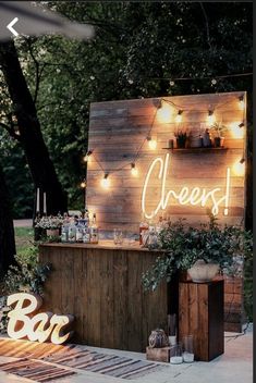 an outdoor bar is decorated with lights and greenery on the outside, along with wooden letters that spell out cheers