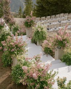 an outdoor wedding setup with white linen and pink flowers in planters on either side of the aisle