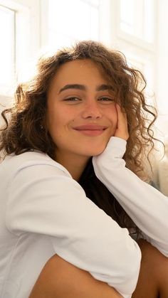 a woman sitting on the floor with her hand under her chin and smiling at the camera