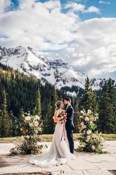 a bride and groom standing in front of mountains with flowers on the ground at their wedding ceremony