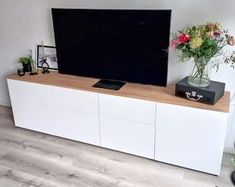 a flat screen tv sitting on top of a white entertainment center next to a vase with flowers