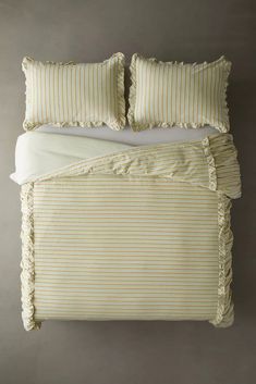 a bed with yellow and white striped comforter on it's side, along with two pillows