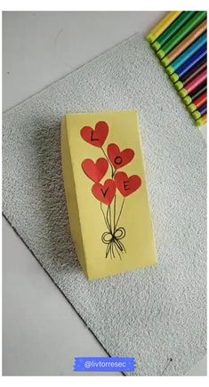 a card with hearts attached to it sitting on the floor next to colored pencils