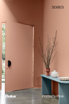 a vase with some flowers in it on a table next to a pink wall and door