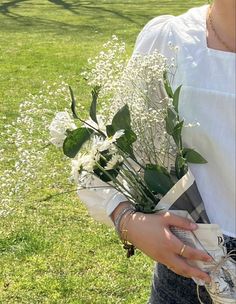 a woman holding a bouquet of flowers in her hands on the grass outside with trees