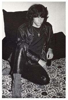 a young man sitting on top of a bed next to a bottle of wine and wearing boots