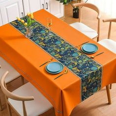 an orange table cloth with blue plates and flowers on it is sitting in front of a white cabinet