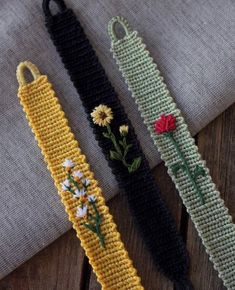 three crocheted bracelets with flowers on them sitting on top of a wooden table