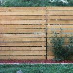 a wooden fence that is next to a car in the yard with grass and bushes