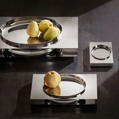 two silver plates with apples in them sitting on a table next to another plate that is shaped like a bowl