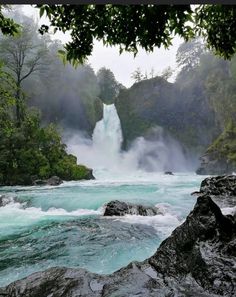 the water is blue and green as it pours into the river from behind some rocks