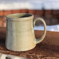 a ceramic mug sitting on top of a wooden table next to snow covered ground and trees