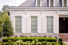 a house with white shutters and trimmed hedges