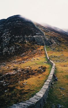 two people sitting on the side of a hill with a stone wall in front of them