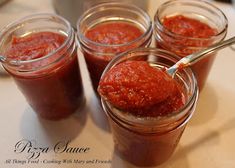 four jars filled with sauce sitting on top of a table