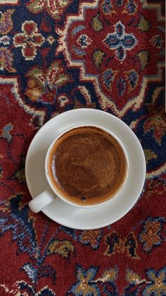 a cup of coffee on top of a saucer in front of a red rug