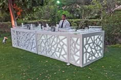 a man standing at a bar with glasses on it in the grass next to trees