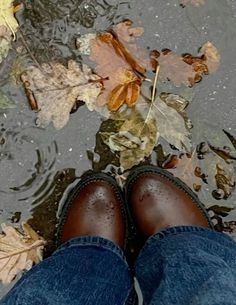 a person's feet standing in the water with leaves on the ground next to them