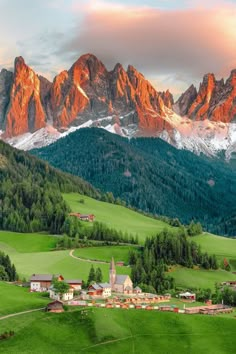 the mountains are covered in snow and green grass, with houses on either side of them