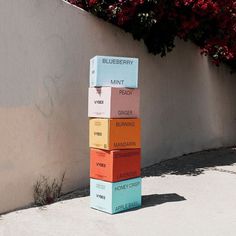 a stack of colorful boxes sitting on top of a cement ground next to a wall