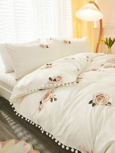 the comforter is white with pink roses on it and pom - poms