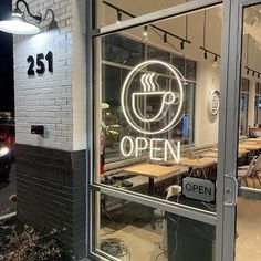 an open sign on the window of a coffee shop with tables and chairs in the background