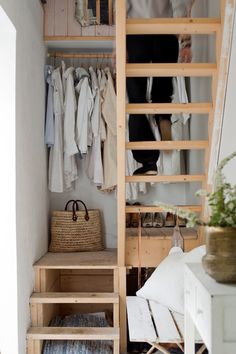 an open closet with clothes hanging on the wall and a ladder leading up to it