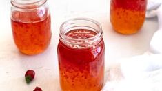 two jars filled with liquid sitting on top of a white table next to strawberries