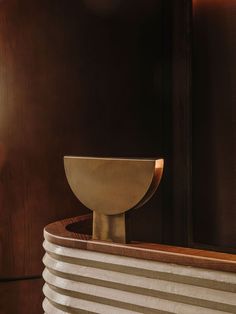 a gold bowl sitting on top of a white pedestal in front of a wooden wall