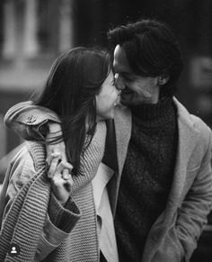 a man and woman kissing each other while walking down the street in black and white