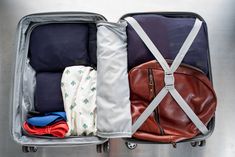 an open suitcase with clothes and other items in it, sitting on a metal surface