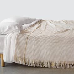 an unmade bed with white sheets and blankets on it's headboard, next to a wooden foot board