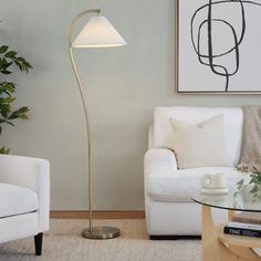 a living room with two white chairs and a lamp on the table in front of it