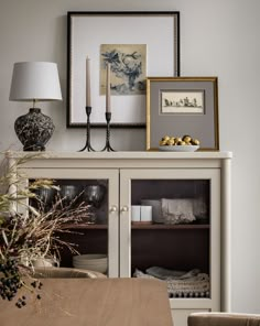 a dining room table with two vases on top of it and pictures above the hutch