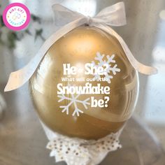 a gold ornament with white snowflakes on it that says he she what will our true snowflake be?