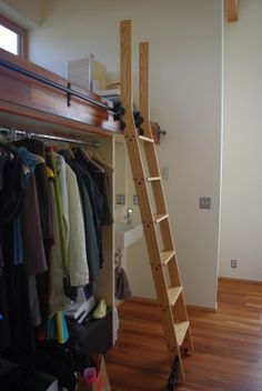 there is a ladder leaning against the wall next to clothes on hangers in this closet