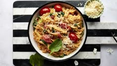 a bowl of pasta with tomatoes, cheese and spinach on a black and white striped place mat