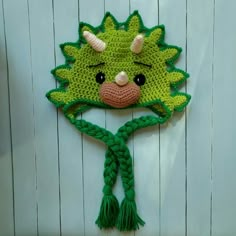 a crocheted green hat with horns and braids hanging on a white wall