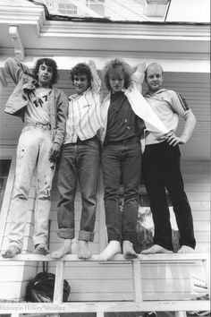 an old black and white photo of four people standing on a porch with their arms around each other