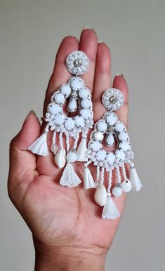 "Bohemian handmade embellished white cabochons and raffia fringes statement weddingid size earrings. The earrings are purely handmade and handcrafted using white acrylic cabochons, raffia, shell, cowrie, pompoms, handmade beads, glass beads, brass, acrylic, and many elements with and accent of silver gold. The earrings are ideal wedding jewelry and measure about approx. 3\" long with the charms hanging and 1.70\" wide. Available in two accent color: Gold accent Silver accent PS: Carnation jewelr Handmade Bohemian Bridal Earrings For Party, Elegant Summer Chandelier Earrings, Bohemian Bridal Earrings For Wedding, Elegant White Summer Earrings, Handmade Chandelier Earrings For Wedding, White Teardrop Jewelry For Party, Elegant White Chandelier Earrings For Summer, Handmade Dangle Bridal Earrings, White Handmade Drop Earrings