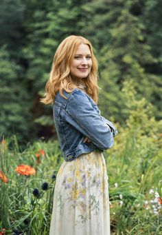 a woman standing in a field with her arms crossed and looking off to the side