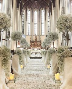 an indoor wedding ceremony with white flowers and candles in front of the alter, surrounded by tall trees