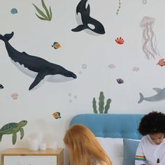 two children sitting on a bed in front of a wall with sea animals and jelly fish